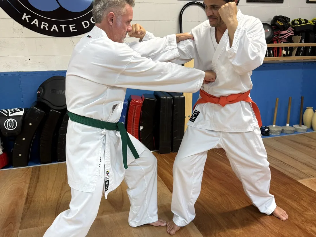 Two students doing controlled partner work at Yushukan Karate, Yushukan logo on the wall behind them