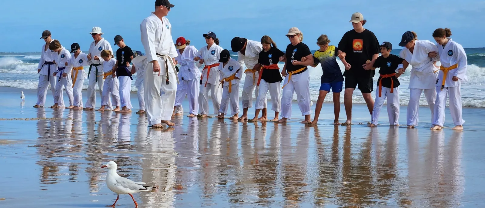 Yushukan Karate students of all ages training on the beach, gi on, lined up along the water's edge